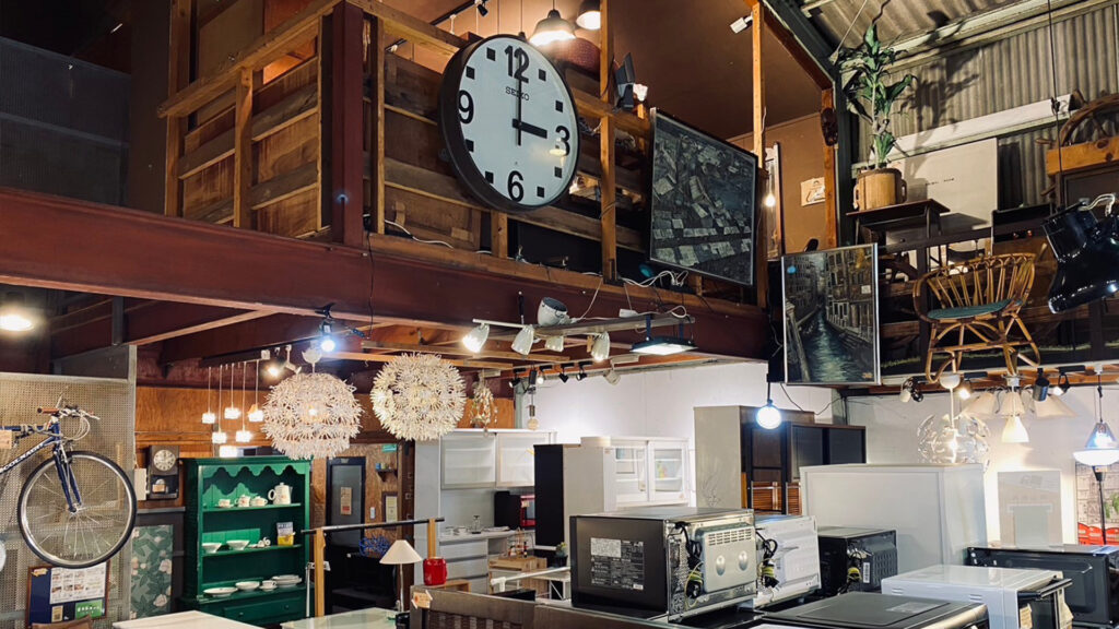 倉敷市のリサイクルショップ「キミドリ倉敷松島店」の店内画像。家具や家電製品がおしゃれな照明に照らされている。