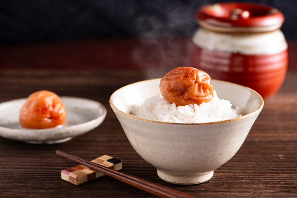 湯気の立つ白ご飯の上に乗った梅干し。和食の朝食イメージ